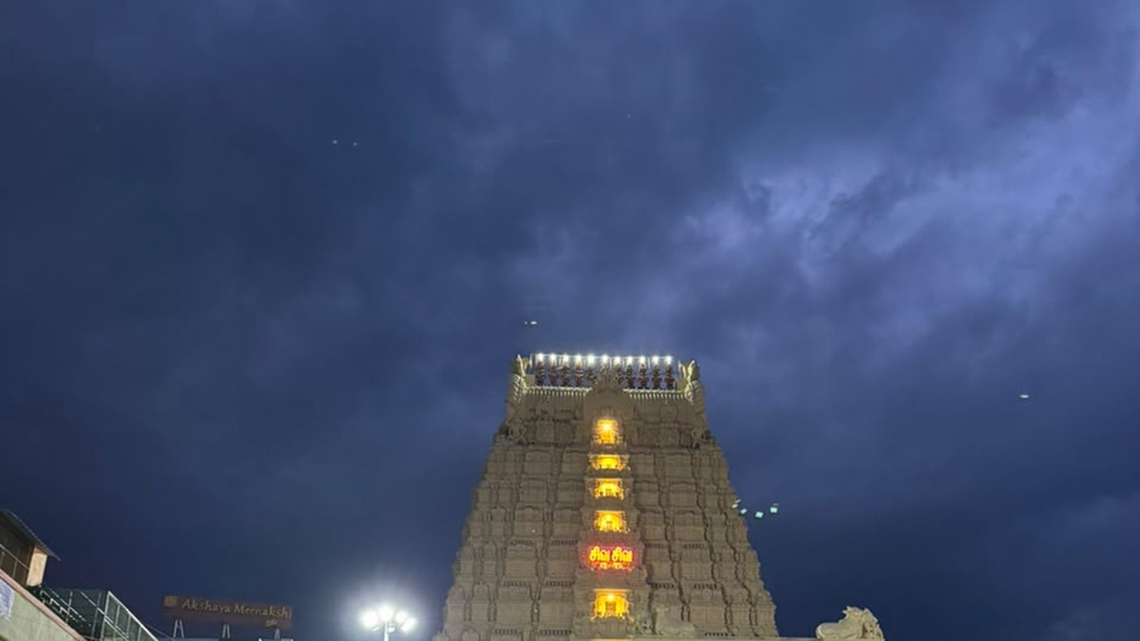 Illuminated temple gopuram rising over a Tamil Nadu temple-town street under a deep dusk sky