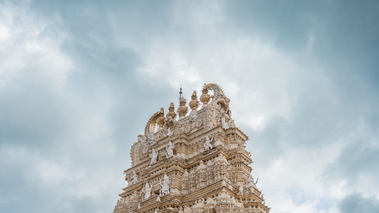 Sandstone-toned South Indian temple gopuram rising against a clouded sky on the Pancha Bhoota Sthalam circuit