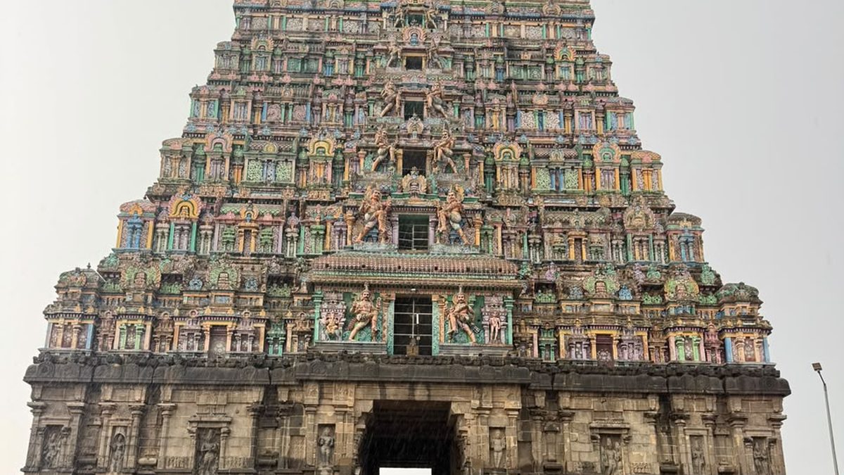 Massive unpainted granite gopuram above a broad paved temple forecourt in Tamil Nadu