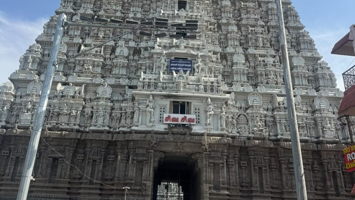 Whitewashed temple gopuram seen from the forecourt beneath a monsoon sky in Tamil Nadu