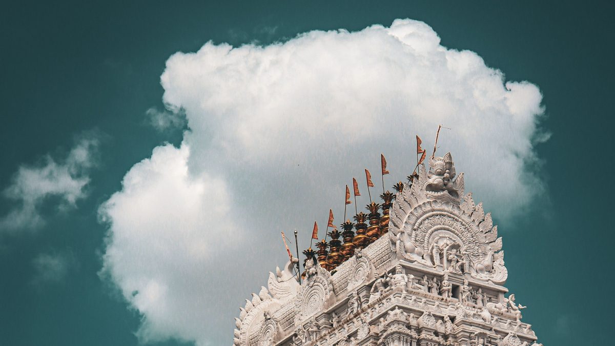 Pale temple gopuram crowned with flagstaffs beside a towering white cloud