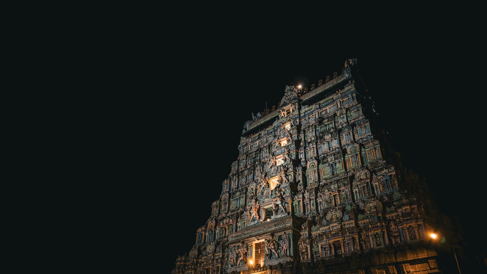 Temple gopuram lit from below standing against a completely black night sky