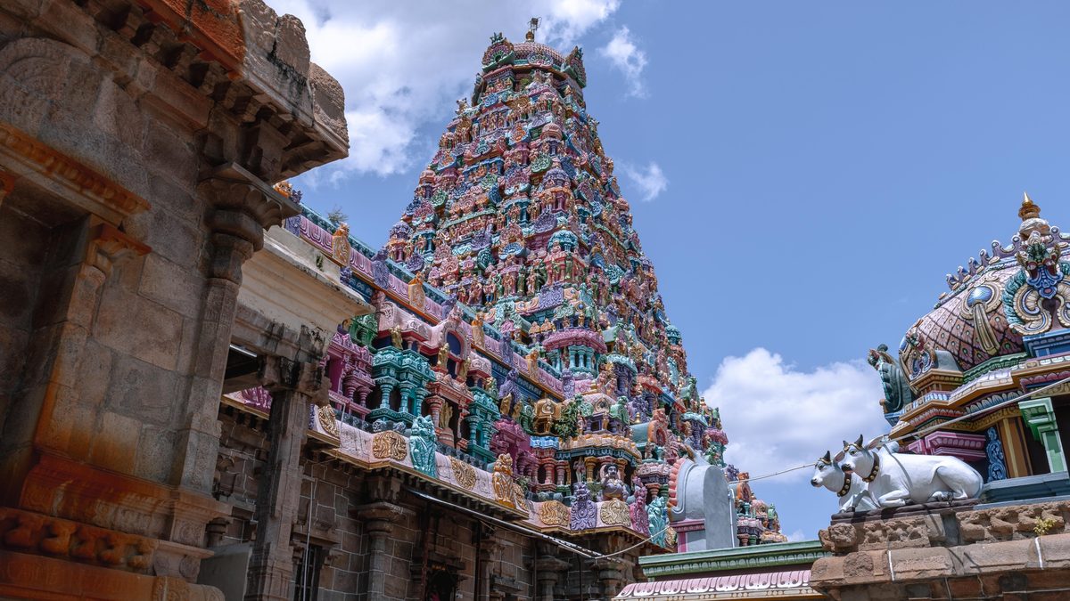 Painted temple gopuram framed by the weathered stone edge of a mandapam corridor