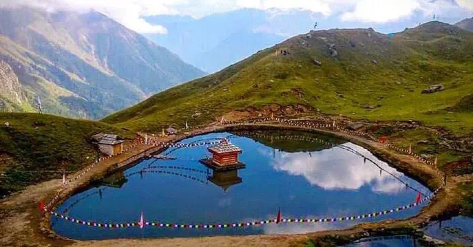 Yulla Kanda glacial lake with snow peaks in the background and the small Krishna temple visible on a rocky outcrop