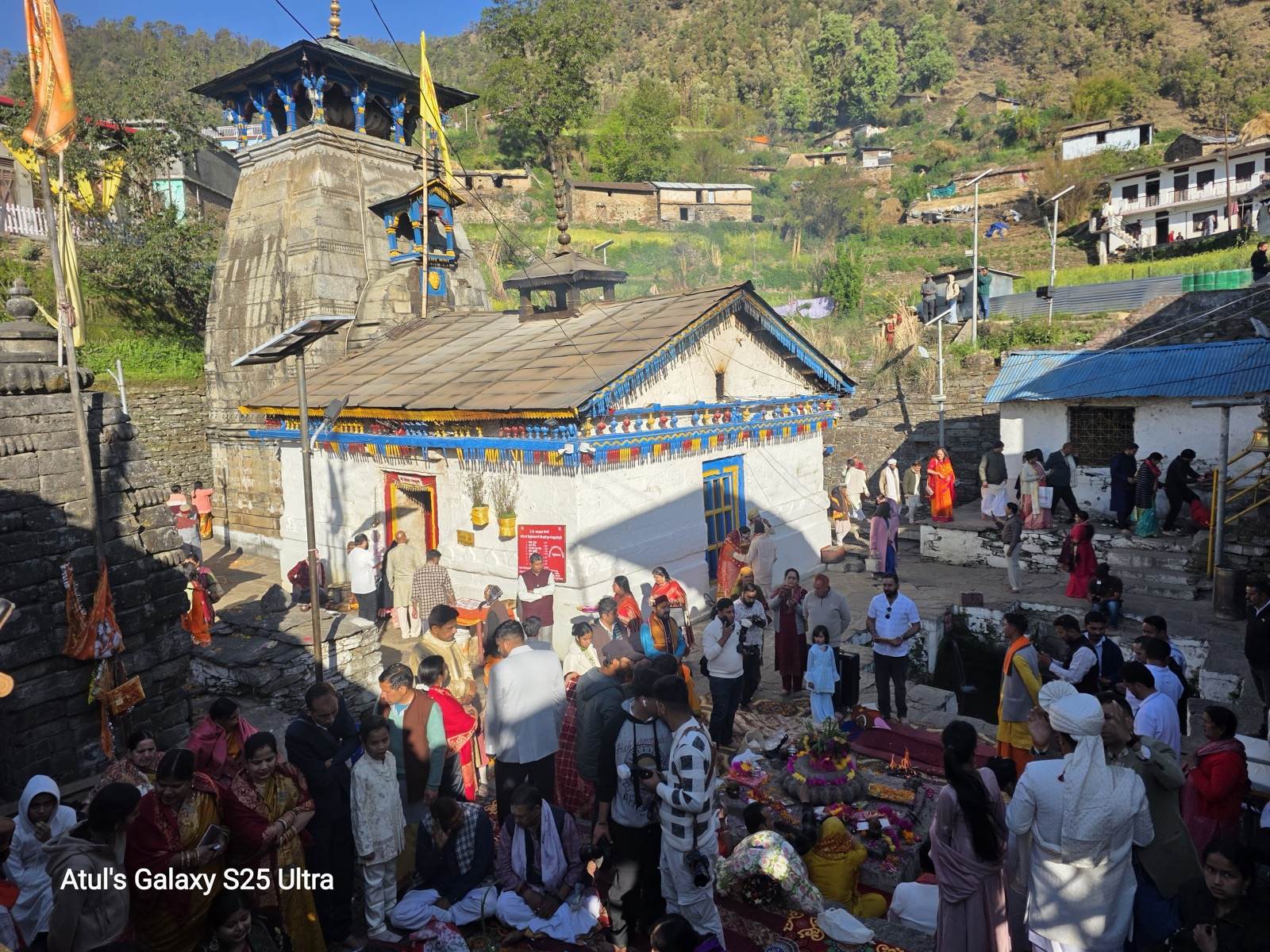 Triyuginarayan Temple with pilgrims gathered in the courtyard on an April morning, Himalayan village in the background