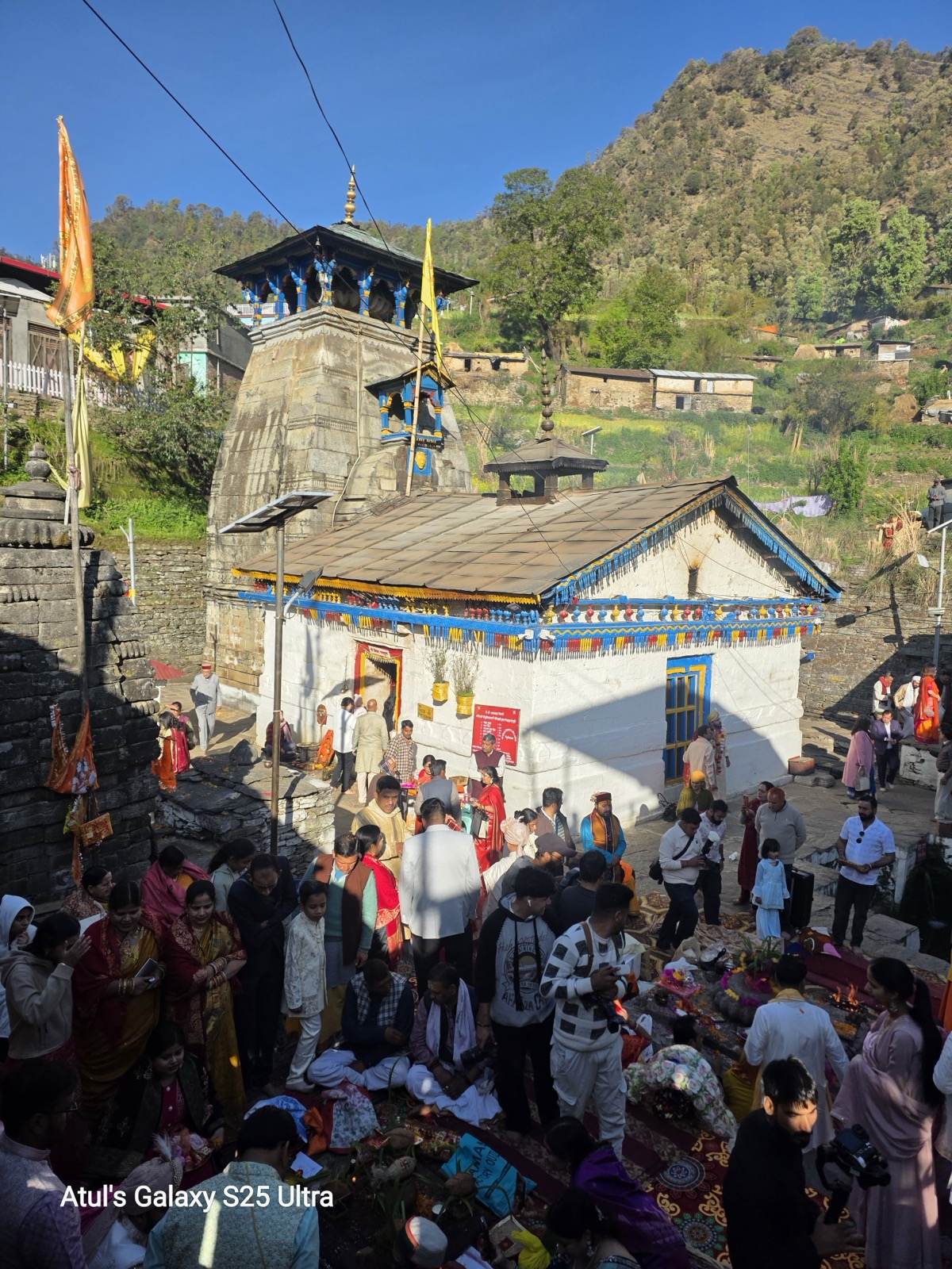 Triyuginarayan Temple stone shikhara with blue and yellow festival trim and pilgrims gathered below