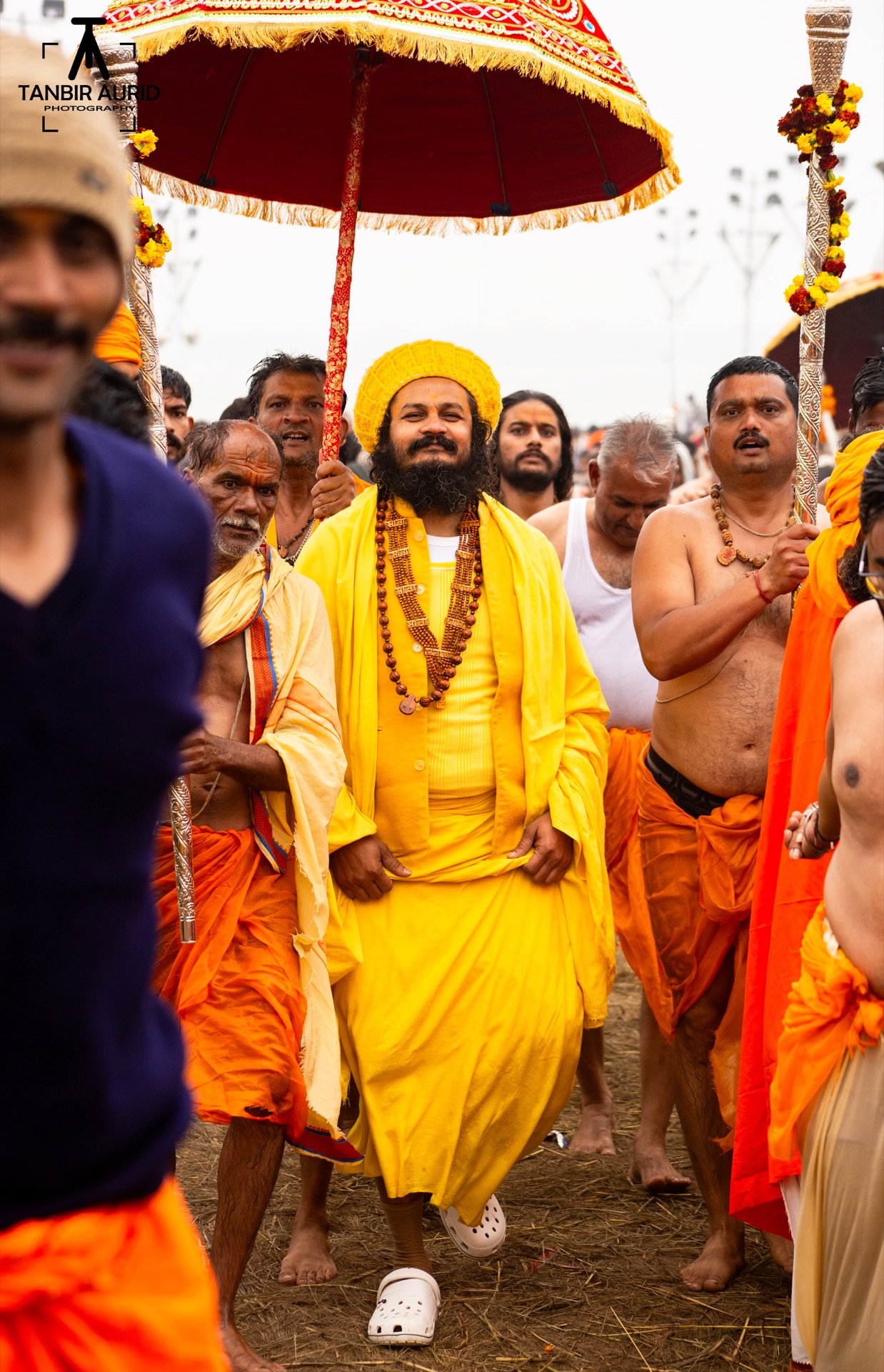 Yogi in yellow robes walking under a ceremonial umbrella during the Peshwai procession