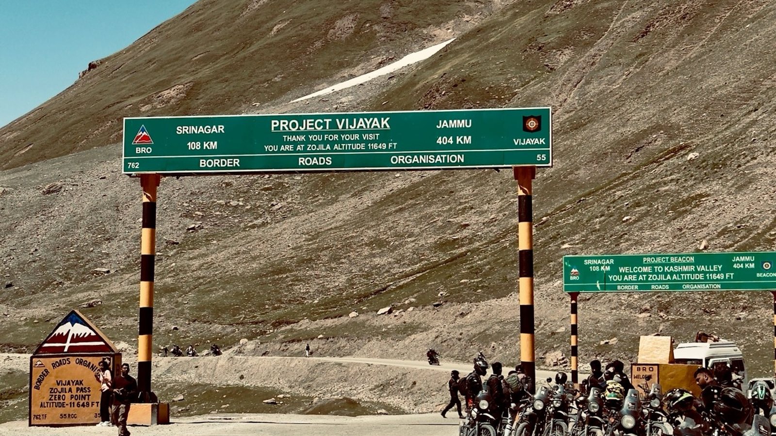 A road signboard at a high pass with motorcycles parked beside it