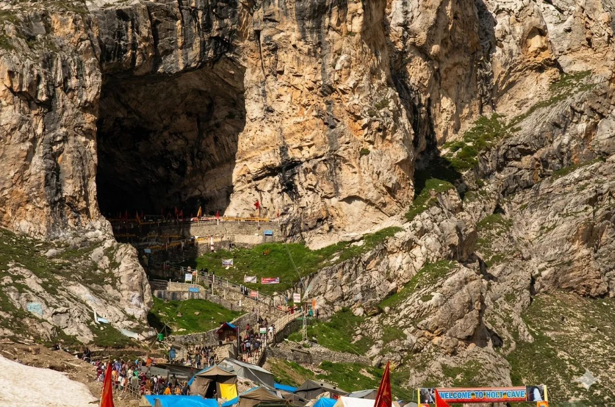Pilgrims approaching the holy Amarnath Cave shrine set in a towering rock face, with tents and prayer flags on the trail below