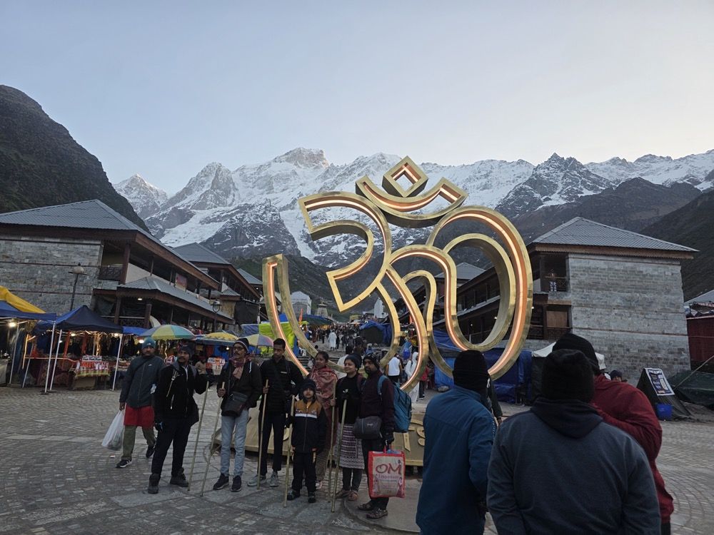 Golden Om sculpture at Kedarnath with Himalayan snow peaks at dawn